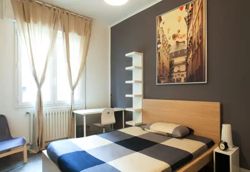 Bright, modern bedroom with a double bed, bedside table, desk by the window and tasteful wall art. Natural light and neutral tones create a comfortable, welcoming atmosphere.