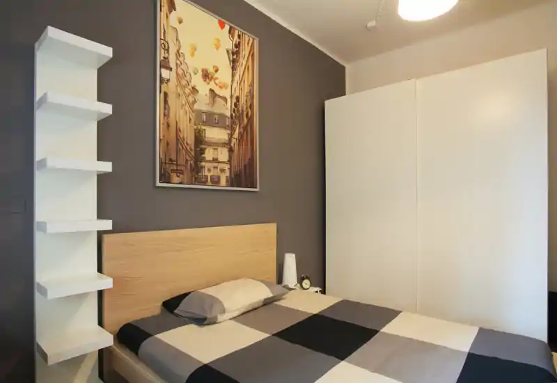 Bright, modern bedroom with a double bed featuring a geometric duvet, a wooden headboard, white wardrobe and decorative wall art. The room is neatly styled and well lit — ideal for rental photos.