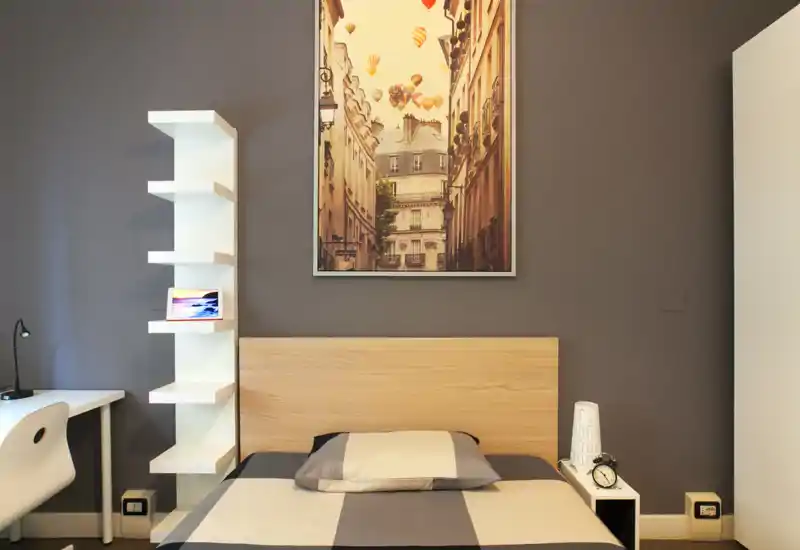 Bright, contemporary bedroom with a neatly made double bed, minimalist shelving and a framed city artwork above the headboard — calm, well-staged and photo-ready.
