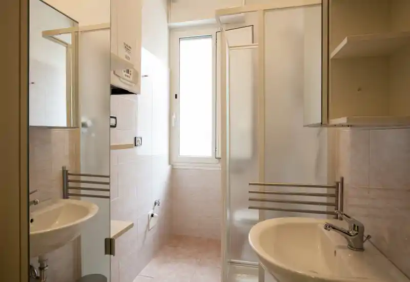 Compact, well-lit bathroom with a sink, mirror, tiled walls and a shower cubicle; neutral tones and practical fixtures ideal for a rental listing.