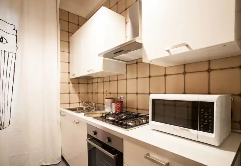 Compact, modern kitchen with gas hob, built-in oven, microwave and sink. Warm tiled backsplash and tidy styling make it practical and inviting for short-term rentals.