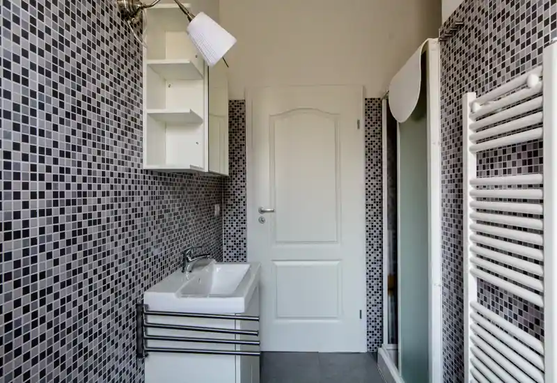 Bagno moderno con piastrelle a mosaico grigio, lavabo a parete, pensile con specchio, scaldasalviette e box doccia; sanitari bianchi e finiture pulite.