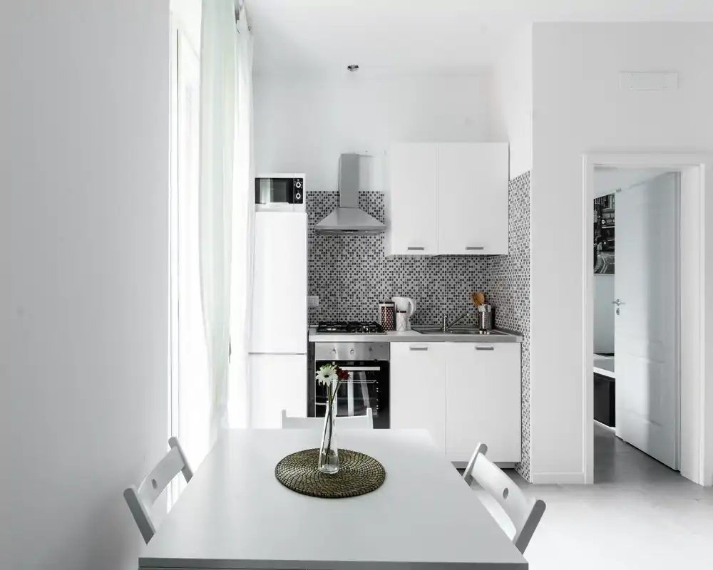 Cocina compacta y moderna con muebles blancos, electrodomésticos de acero y una pequeña mesa de comedor—ideal para un piso urbano.