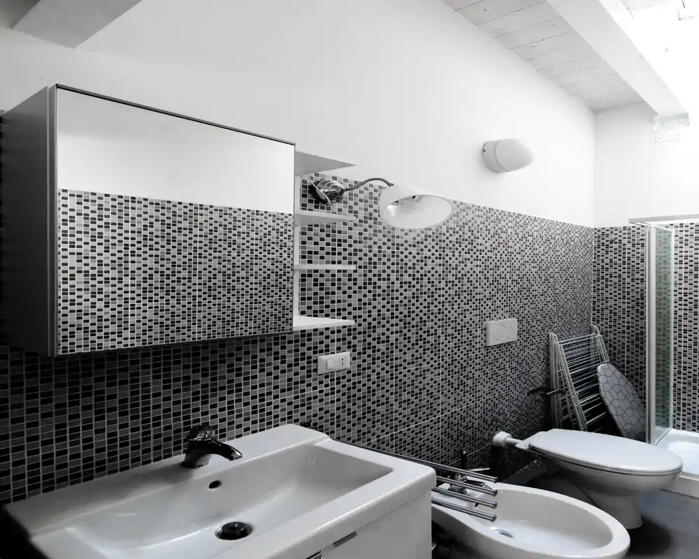 Bagno moderno con pareti in piastrelle mosaico, lavabo con specchiera, bidet e WC e cabina doccia in vetro: disposizione funzionale e arredi contemporanei.