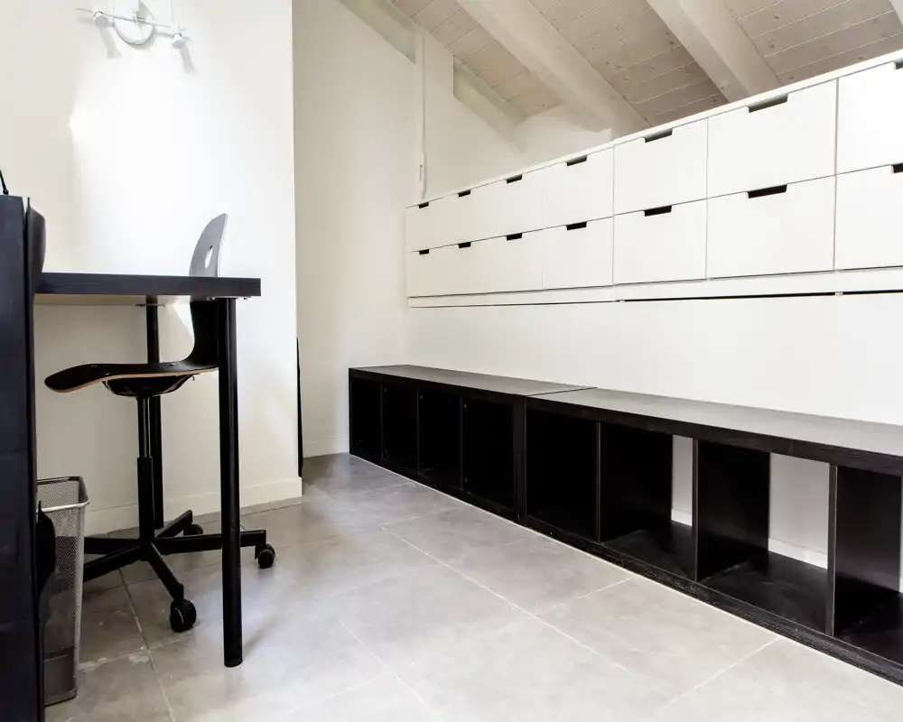 Area living luminosa e minimal con sedute/basi contenitive basse e una piccola scrivania — spazio pulito, moderno e funzionale adatto a uno studio o a un ingresso.