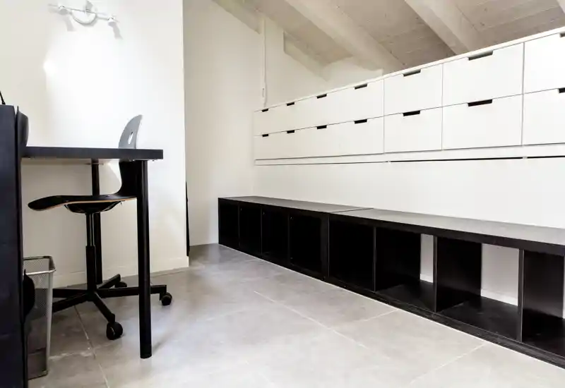 Area living luminosa e minimal con sedute/basi contenitive basse e una piccola scrivania — spazio pulito, moderno e funzionale adatto a uno studio o a un ingresso.