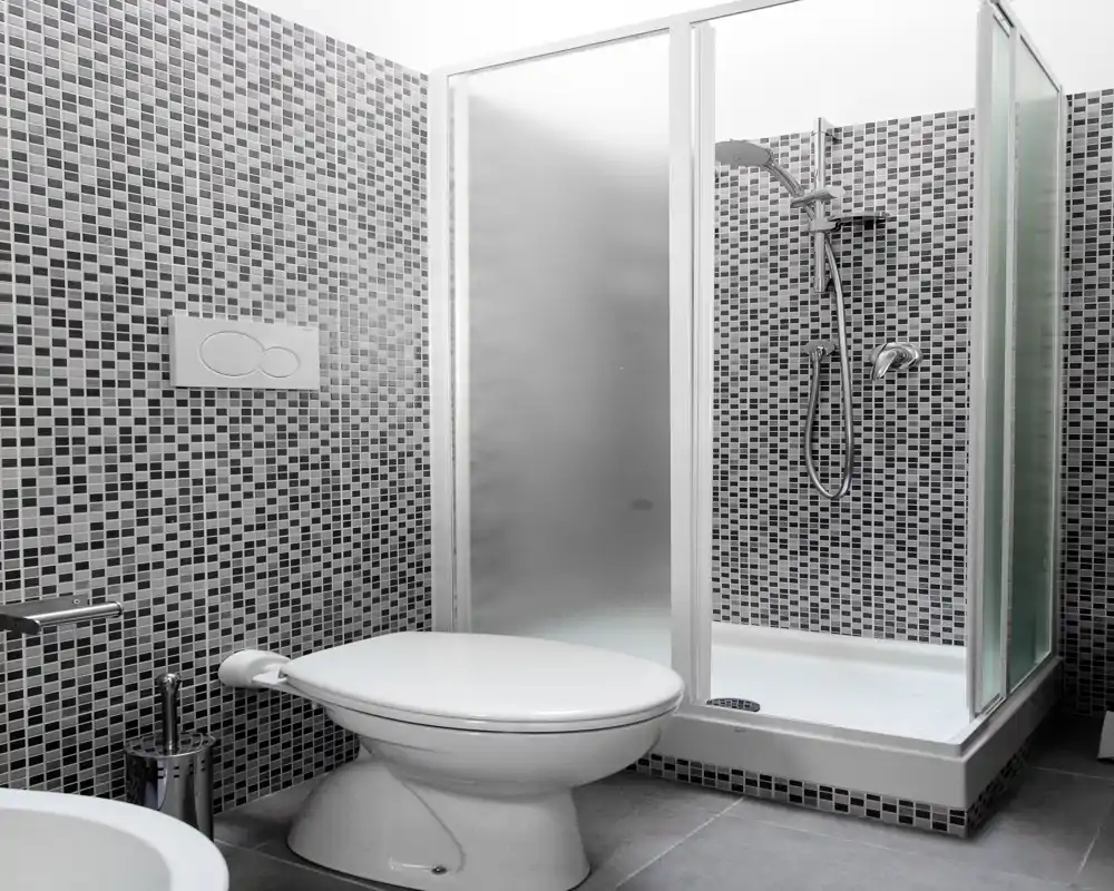 Bagno moderno e compatto con pareti in piastrelle mosaico, box doccia con vetro satinato e wc a parete: pulito e funzionale.