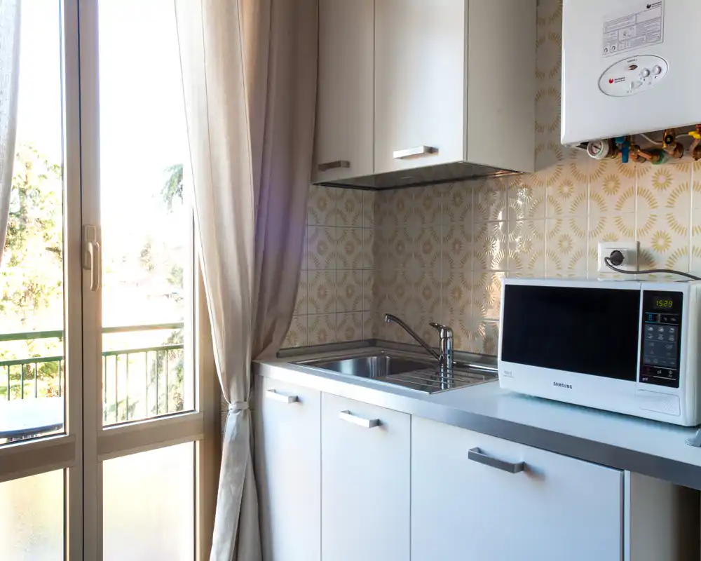 Compact, bright kitchen with patterned tile backsplash, stainless sink and microwave, plus a balcony door that provides natural light.