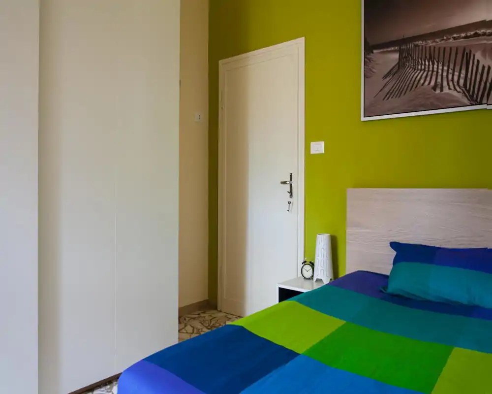 Coin chambre moderne et lumineux avec tête de lit en bois, literie bleu-vert colorée et table de chevet avec lampe et réveil — parfait pour un séjour douillet en ville.