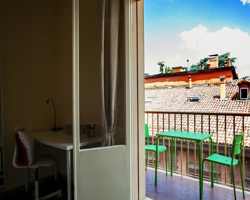 Balcone soleggiato con un piccolo tavolo e sedie verdi che si affacciano sui tetti in cotto — un angolo luminoso per rilassarsi o prendere un caffè.