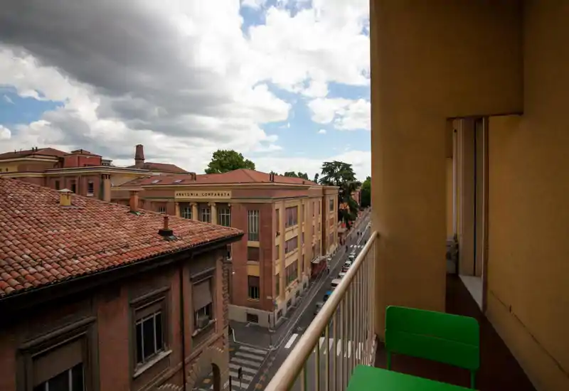 Balcone con vista sui tetti in cotto e una tranquilla strada cittadina, dotato di corrimano e due sedie verdi — perfetto per un caffè mattutino e osservare la città.