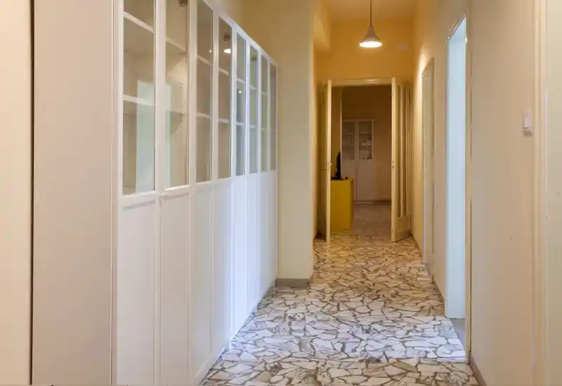 Ingresso/corridoio luminoso e ordinato con armadi a muro bianchi e pavimento in graniglia, che conduce alle stanze interne; illuminazione calda e pareti neutre rendono l’ingresso accogliente.