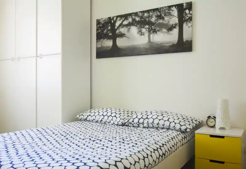 Dormitorio moderno y luminoso con cama doble, ropa de cama estampada, armario empotrado y mesita amarilla. Espacio sencillo y bien iluminado, ideal para alquileres temporales.