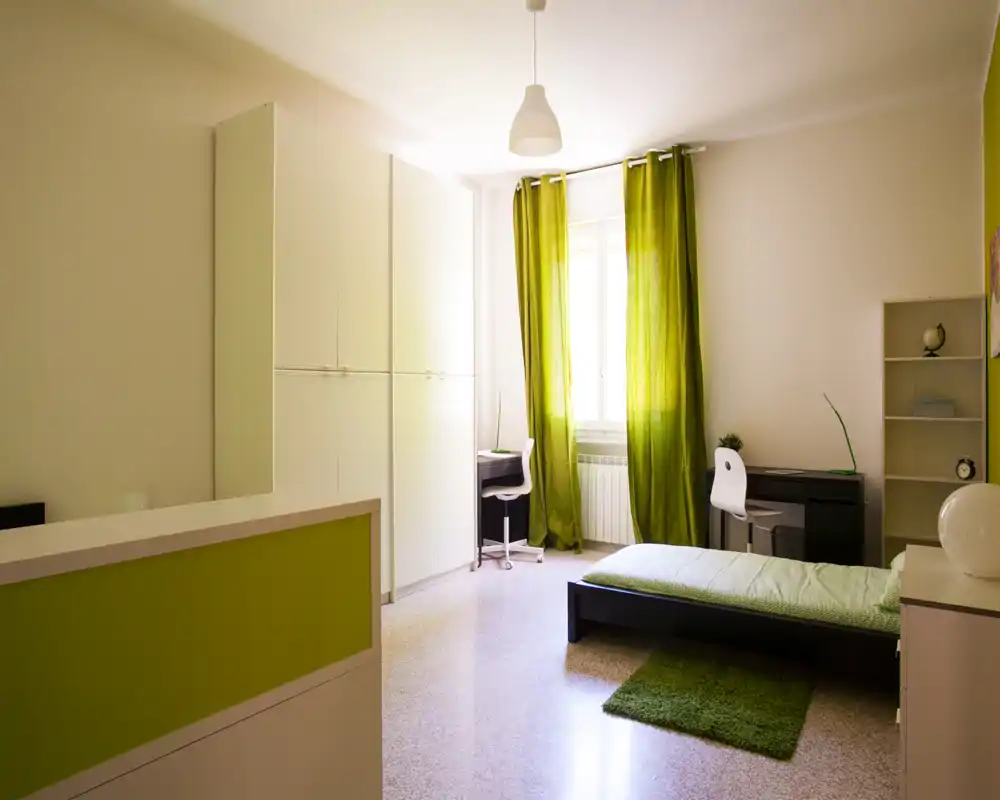 Camera da letto luminosa e moderna con dettagli verdi: letto singolo, scrittoio vicino alla finestra, armadio e piccolo tappeto — ariosa e ben illuminata.
