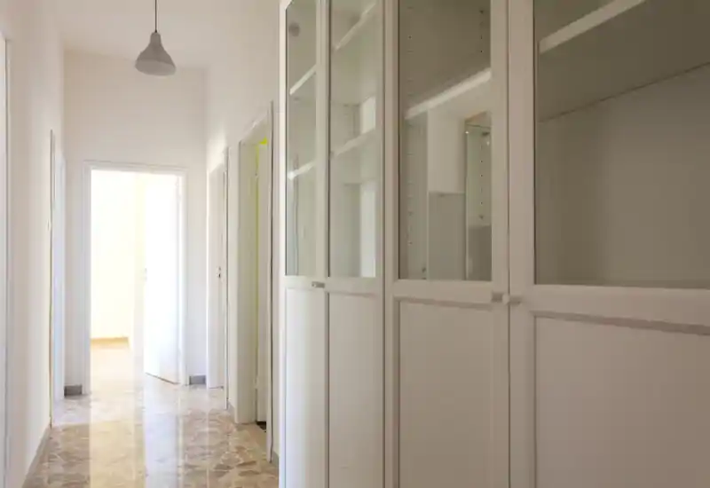 Bright entrance corridor with built-in white storage cabinets and a pendant light, polished patterned floor and clear access to adjacent rooms—ideal as a welcoming hallway.