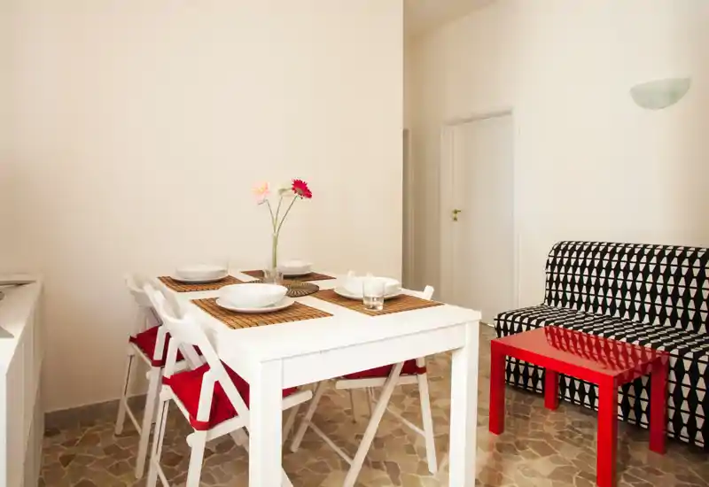 Zona giorno luminosa e ben arredata con un tavolo bianco per quattro, divano con motivo geometrico e tavolino rosso — perfetta per soggiorni in città.
