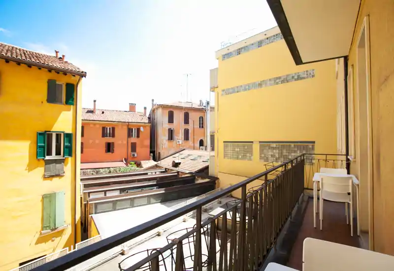 Sunny balcony overlooking colorful historic buildings; small outdoor seating with table and chairs, ideal for morning coffee.