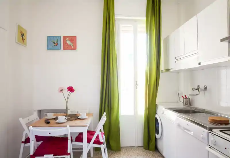 Bright, compact kitchen with a small dining table, cheerful green curtains and white cabinets — ideal for a cozy city apartment.