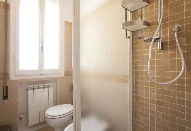 Bright, tidy bathroom with a glass shower cubicle, modern showerhead and a toilet next to a window providing natural light.