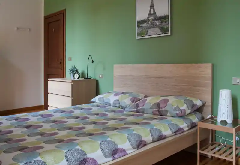 Camera da letto luminosa e ben arredata con ampio letto in legno, copriletto decorato e cuscini coordinati; comodini e illuminazione soffusa creano un’atmosfera accogliente.