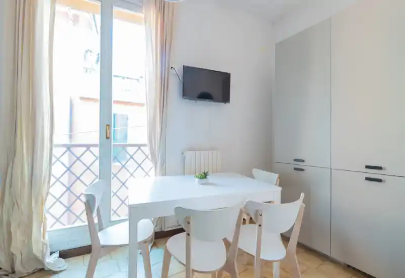 Angolo pranzo luminoso e moderno con tavolo bianco e quattro sedie abbinate, grande finestra/porta verso un piccolo balcone e armadi a muro — perfetto per appartamenti compatti.