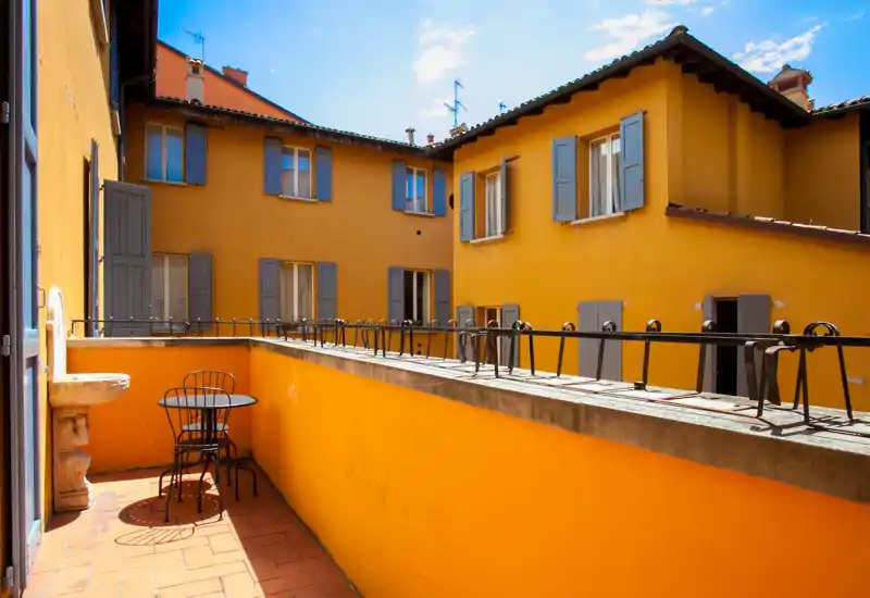 Balcone soleggiato con pavimento in cotto, piccolo tavolino e sedie da bistrot — perfetto per il caffè mattutino e la vista sul cortile.