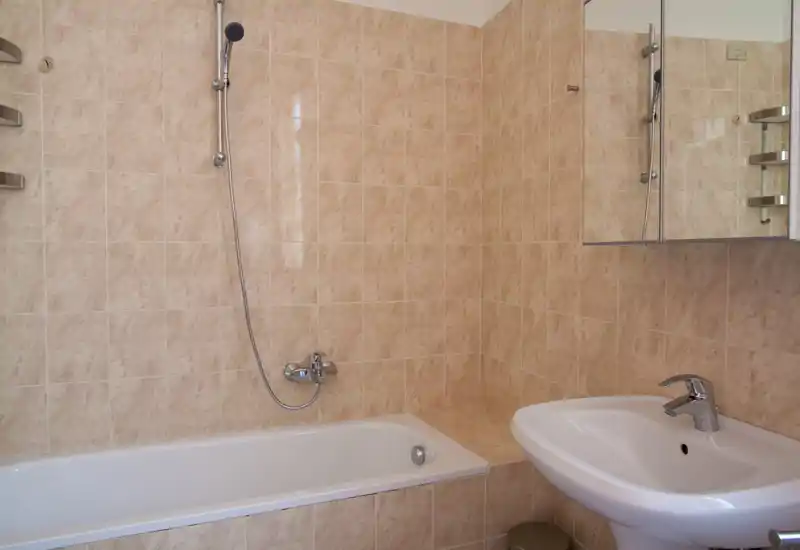 Bagno pulito con vasca, doccia a muro e lavabo; piastrelle beige neutre e mobile con specchio che rendono l'ambiente luminoso e funzionale.