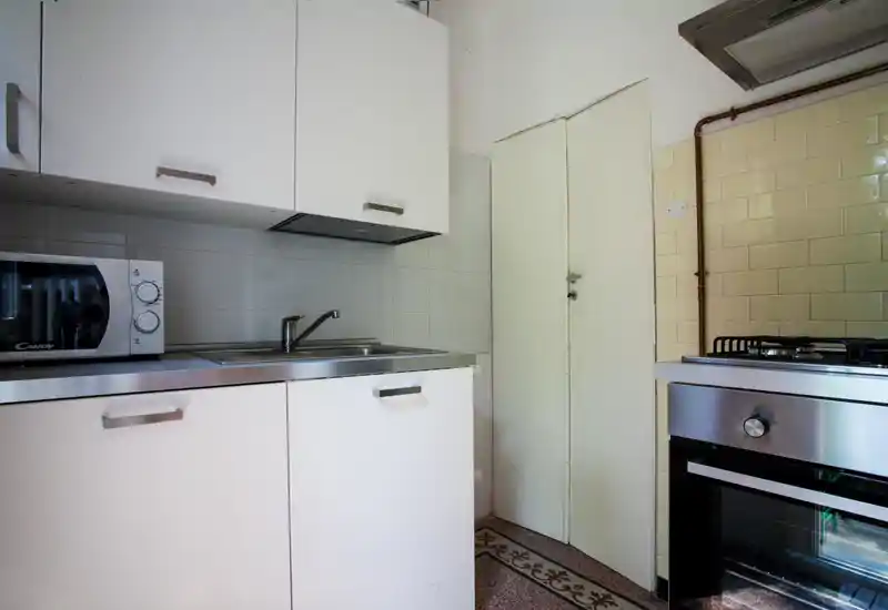 Compact modern kitchen with white cabinets, stainless steel countertop and built-in oven and microwave; clean, functional space with tiled backsplash.