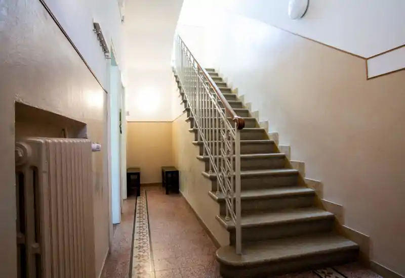 Bright, well-maintained entrance hallway with a tiled floor, radiator, and a staircase with a wooden handrail leading up. Clean lines and soft lighting create a welcoming first impression.