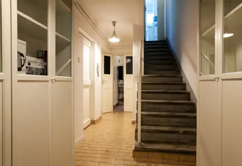 Entry hallway with a tiled floor, built-in cabinets and a staircase leading up. Bright pendant light and white doors create a clean, welcoming feel.