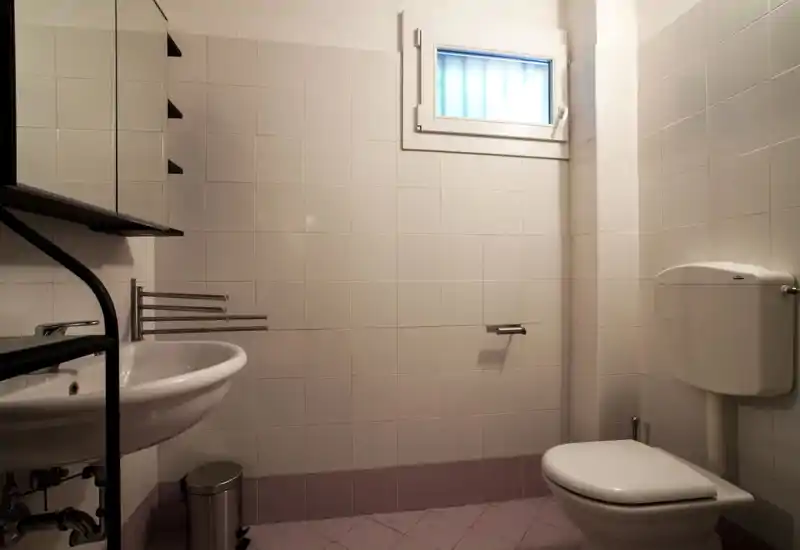 Compact, well-kept bathroom with a wall-mounted sink, mirror cabinet, and toilet; neutral tiles and a small frosted window provide privacy and natural diffused light.