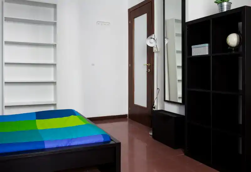 Dormitorio limpio y minimalista con cama doble, estanterías y espejo alto. Espacio luminoso y ordenado, ideal para un anuncio de alquiler.