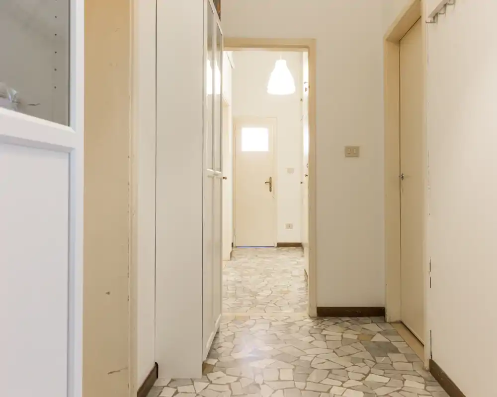 Vestíbulo de entrada luminoso y neutro con suelo de mosaico, armarios empotrados y lámpara colgante — un espacio de entrada limpio y funcional.