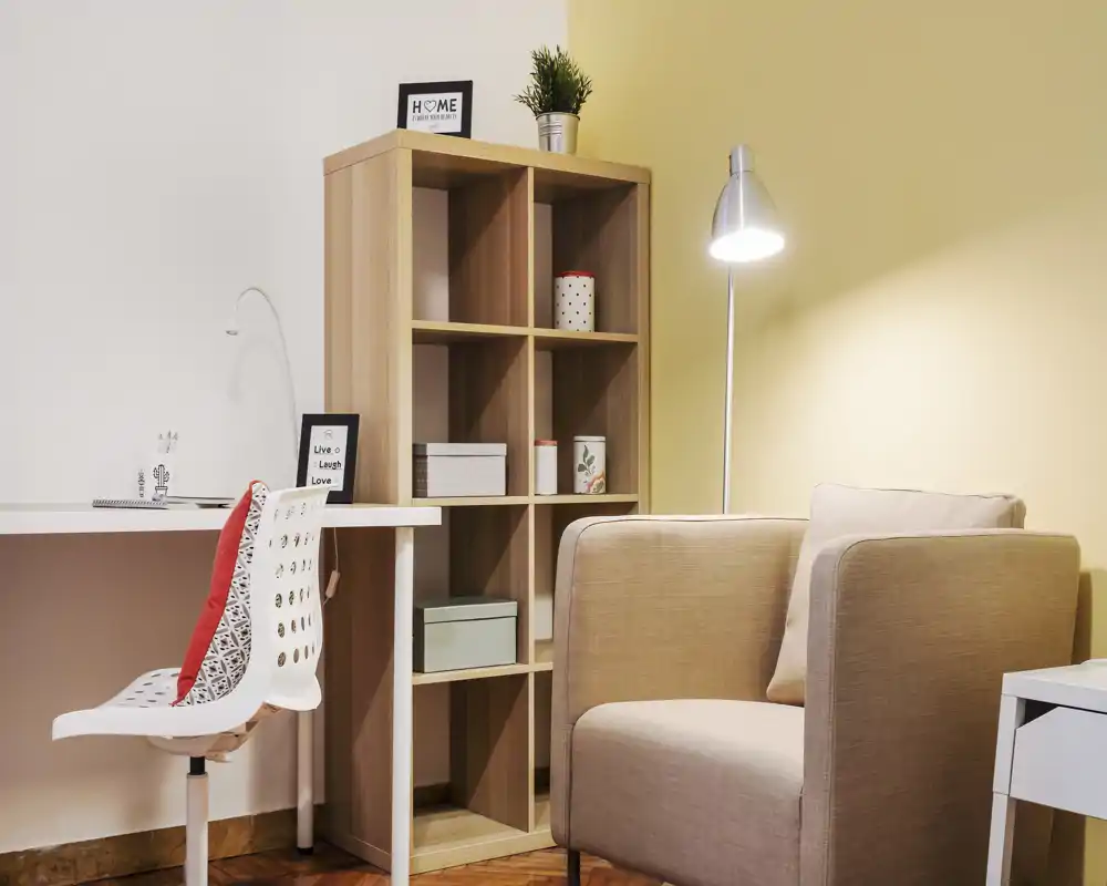 Coin salon chaleureux et bien éclairé avec un fauteuil confortable, une lampe sur pied, une étagère cubique et un petit bureau — idéal pour se détendre ou travailler.