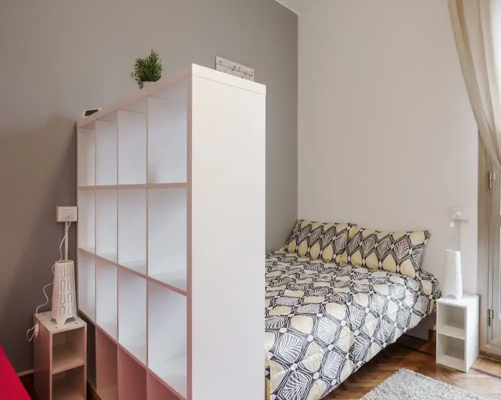 Bright, modern bedroom with a patterned double bed, bedside table and shelving divider that creates a cozy, well-organized sleeping area with natural light.