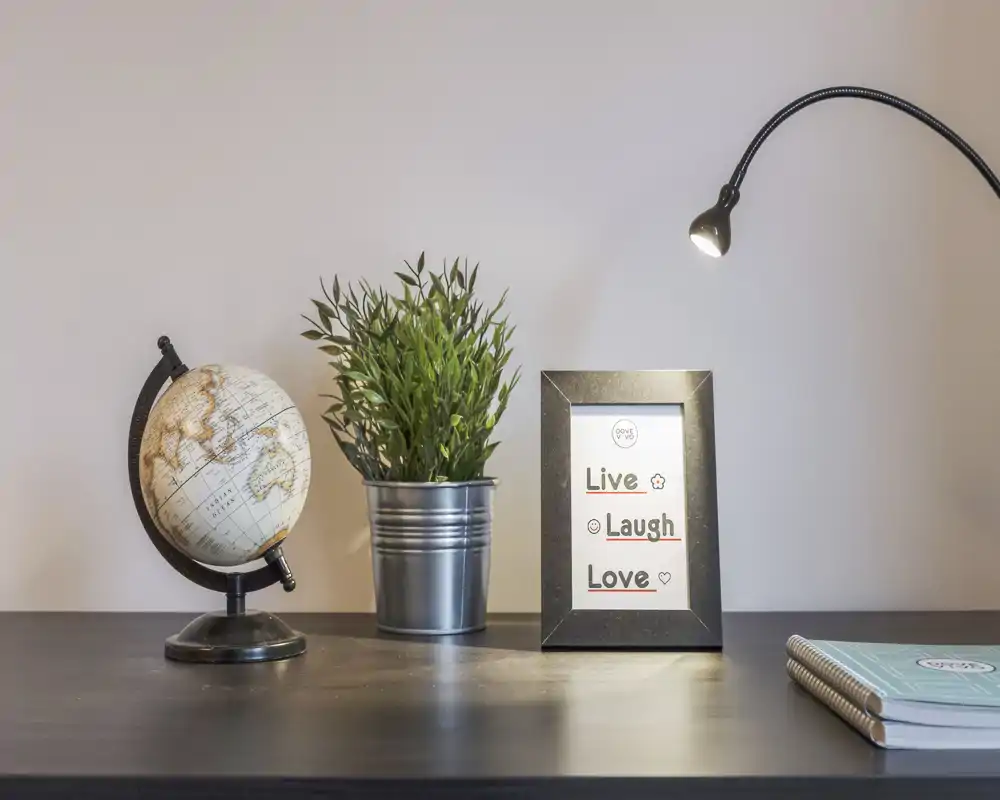 Una scenografia da tavolo ordinata con globo, pianta in vaso, cornice con frase ispiratrice e lampada da scrivania — perfetta per valorizzare un ingresso o una superficie decorata.