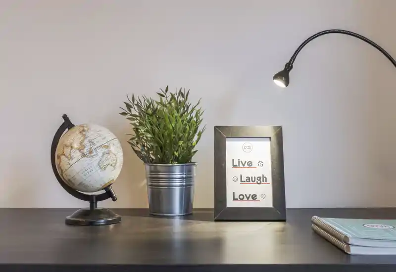 Una scenografia da tavolo ordinata con globo, pianta in vaso, cornice con frase ispiratrice e lampada da scrivania — perfetta per valorizzare un ingresso o una superficie decorata.