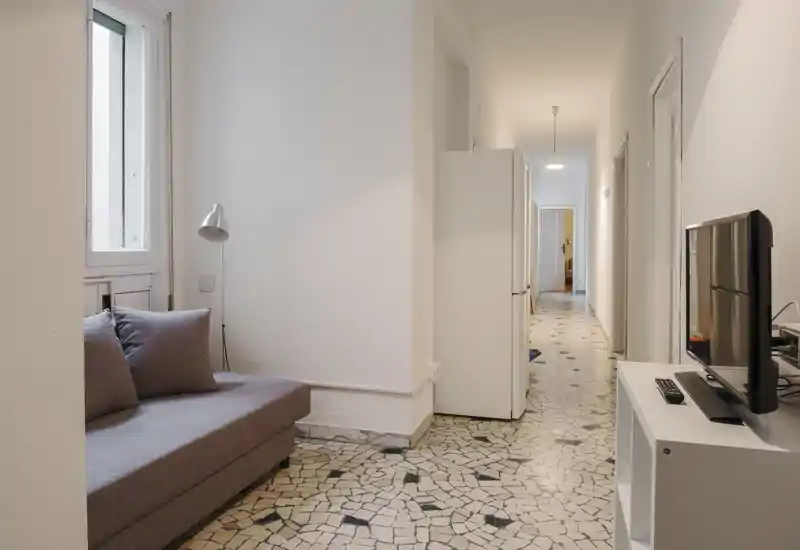 Zona giorno compatta con divano grigio, lampada da terra e TV, in un appartamento luminoso con pavimento in terrazzo a motivi.