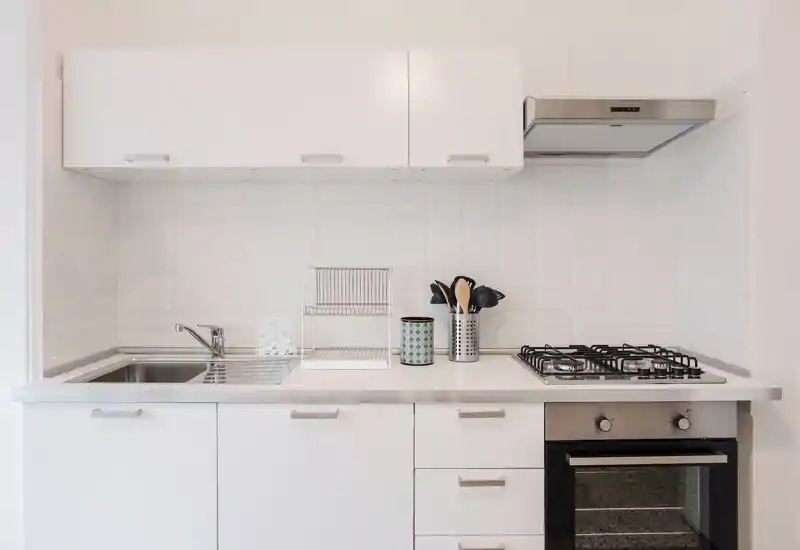 Cucina moderna e compatta, luminosa con pensili bianchi, lavello in acciaio, piano cottura a gas e forno incassato — perfetta per appartamenti in città.