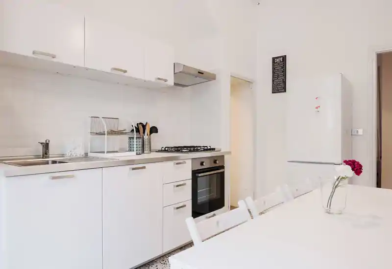 Cucina moderna e luminosa con pensili bianchi, forno incassato e tavolo da pranzo; stile minimal e pulito con luce naturale gradevole.
