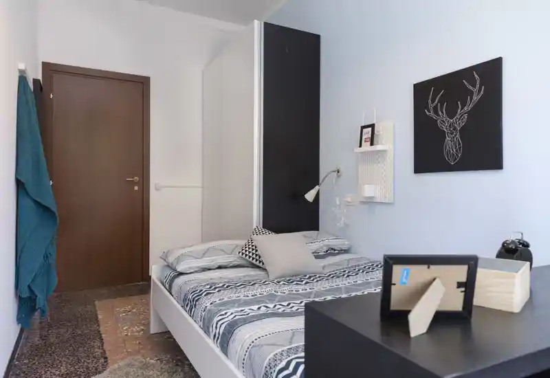 Chambre simple décorée avec couette à motifs, coussins décoratifs, lampe de chevet et tableau mural ; lumineuse, propre et accueillante.