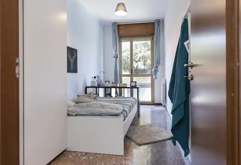 Chambre simple lumineuse et bien rangée avec lit plateforme blanc, literie à motifs, table de chevet et grande fenêtre laissant entrer la lumière naturelle — idéale pour une annonce axée sur le confort et la simplicité moderne.