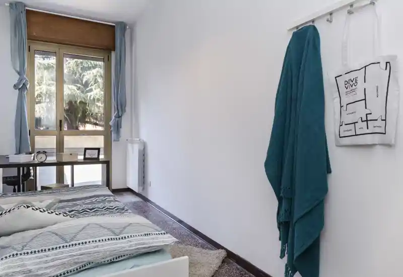 Chambre lumineuse et soignée avec un lit bien fait, grande fenêtre apportant de la lumière naturelle et textiles chaleureux.