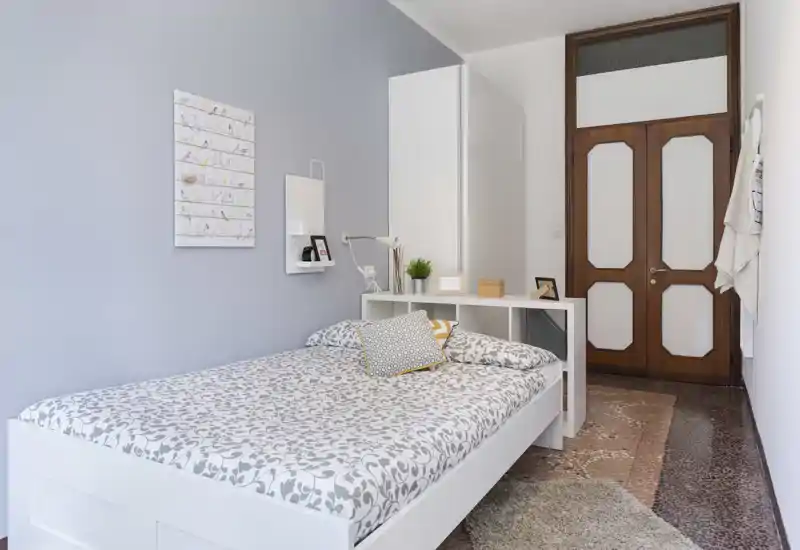 Bright, well-styled bedroom with a patterned double bed, bedside shelf and minimal modern storage—clean lines and soft textiles create a cozy feel.