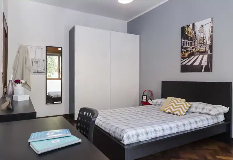 Chambre moderne et lumineuse avec lit double en parure à carreaux, grand placard blanc, bureau et tableau mural — bien mise en scène pour une annonce.