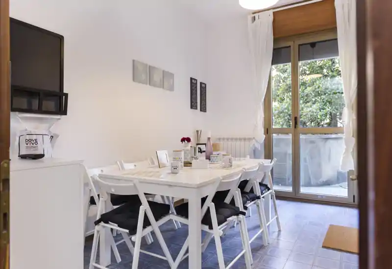 Bright, well-staged dining area with a white table and folding chairs, set near a large window/door that opens to an outdoor space. Ideal for cosy meals and social gatherings.