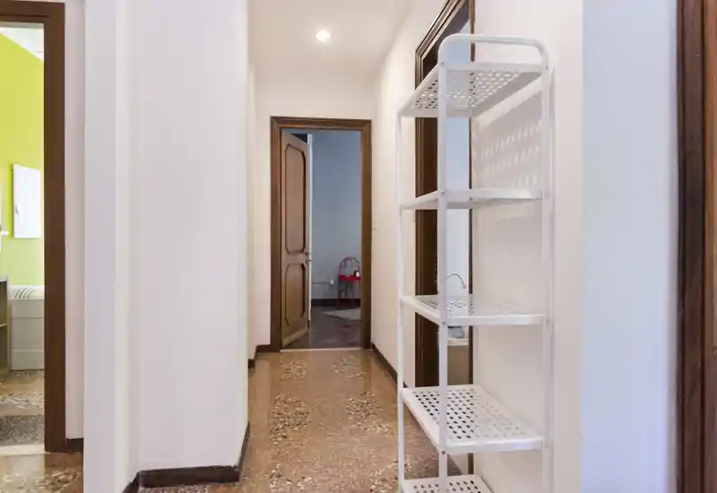 Bright, clean hallway with terrazzo floor, white walls and a simple shelving unit—ideal as an entrance or corridor area connecting rooms.