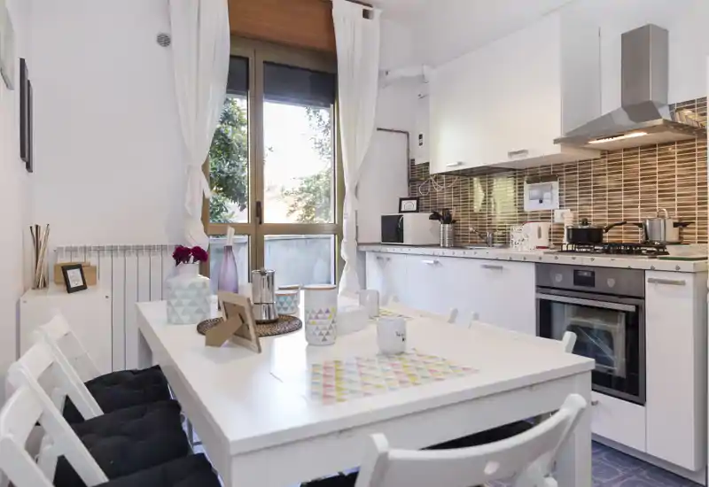 Bright, modern kitchen with integrated oven, gas hob and a dining table set for casual meals. White cabinets and patterned backsplash create a fresh, welcoming space ideal for short-term rentals.