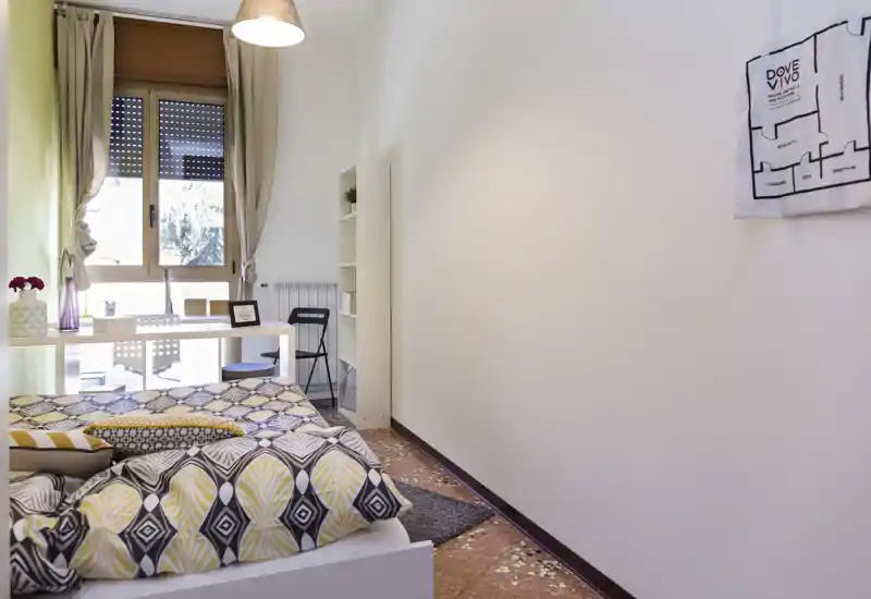 Bright, modern bedroom with patterned bedding, a window-side desk and tasteful decor—ideal for a single occupant or couple.