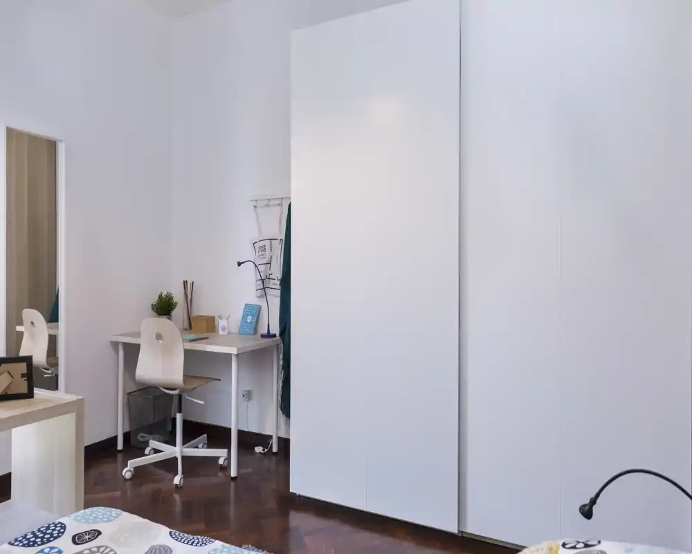Bright, modern bedroom with a visible bed corner, clean white wardrobe and a small study desk—ideal for guests or students.